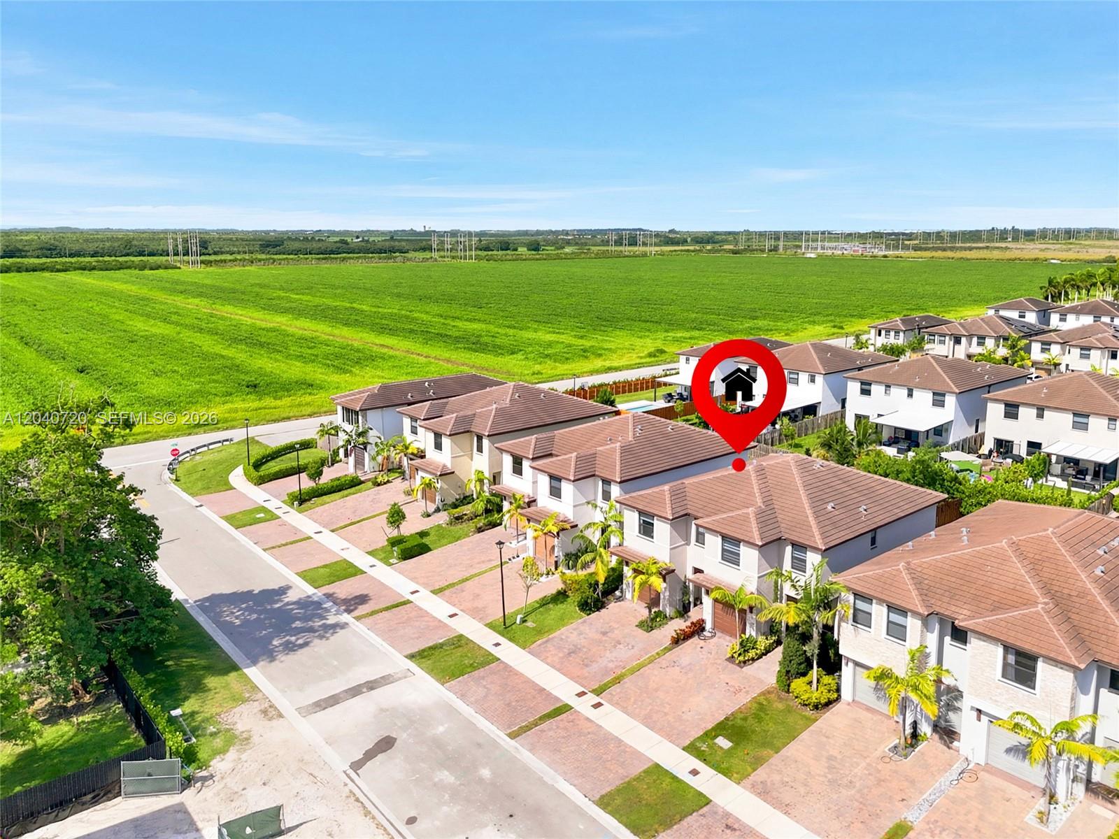 An aerial view shows a row of suburban houses adjacent to a large green field — HOMESTEAD, FL