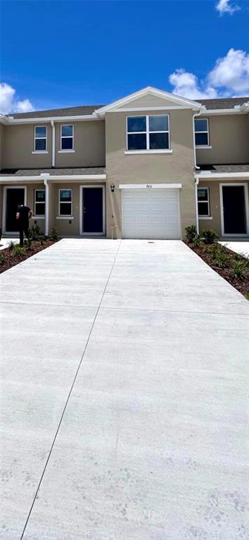 A two-story townhouse exterior features a beige facade, a white garage door, and a driveway — 760 PRESTON COVE DRIVE, ST CLOUD, FL
