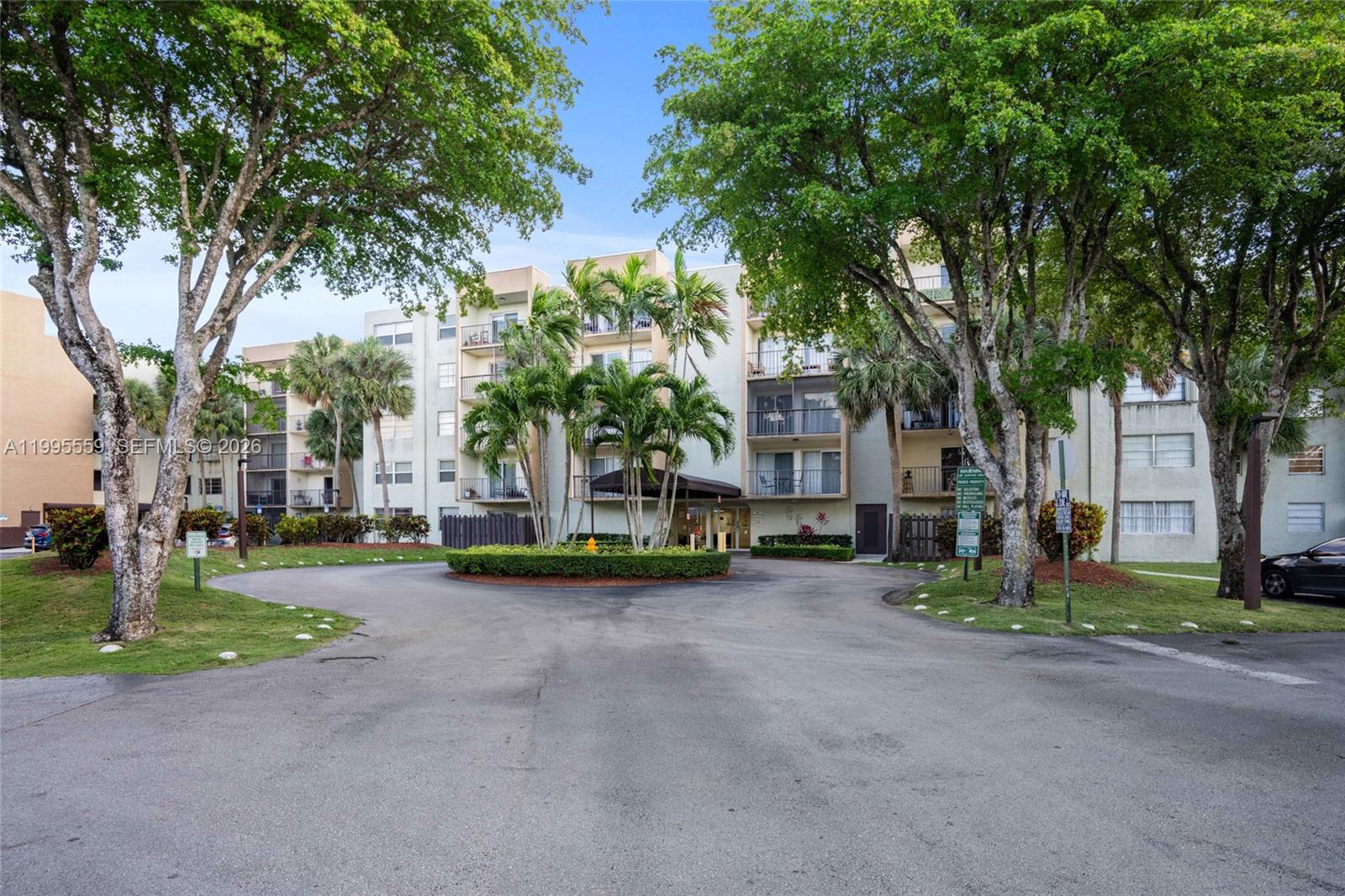 A multi-story apartment building features a circular driveway, palm trees, and mature landscaping — 14250 SW 62nd St # 402, Miami FL 33183, MIAMI, FL