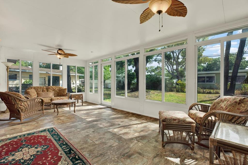 A sunroom features tile flooring, wicker furniture, ceiling fans, and large windows overlooking a yard — 2561 58TH STREET N, ST PETERSBURG, FL