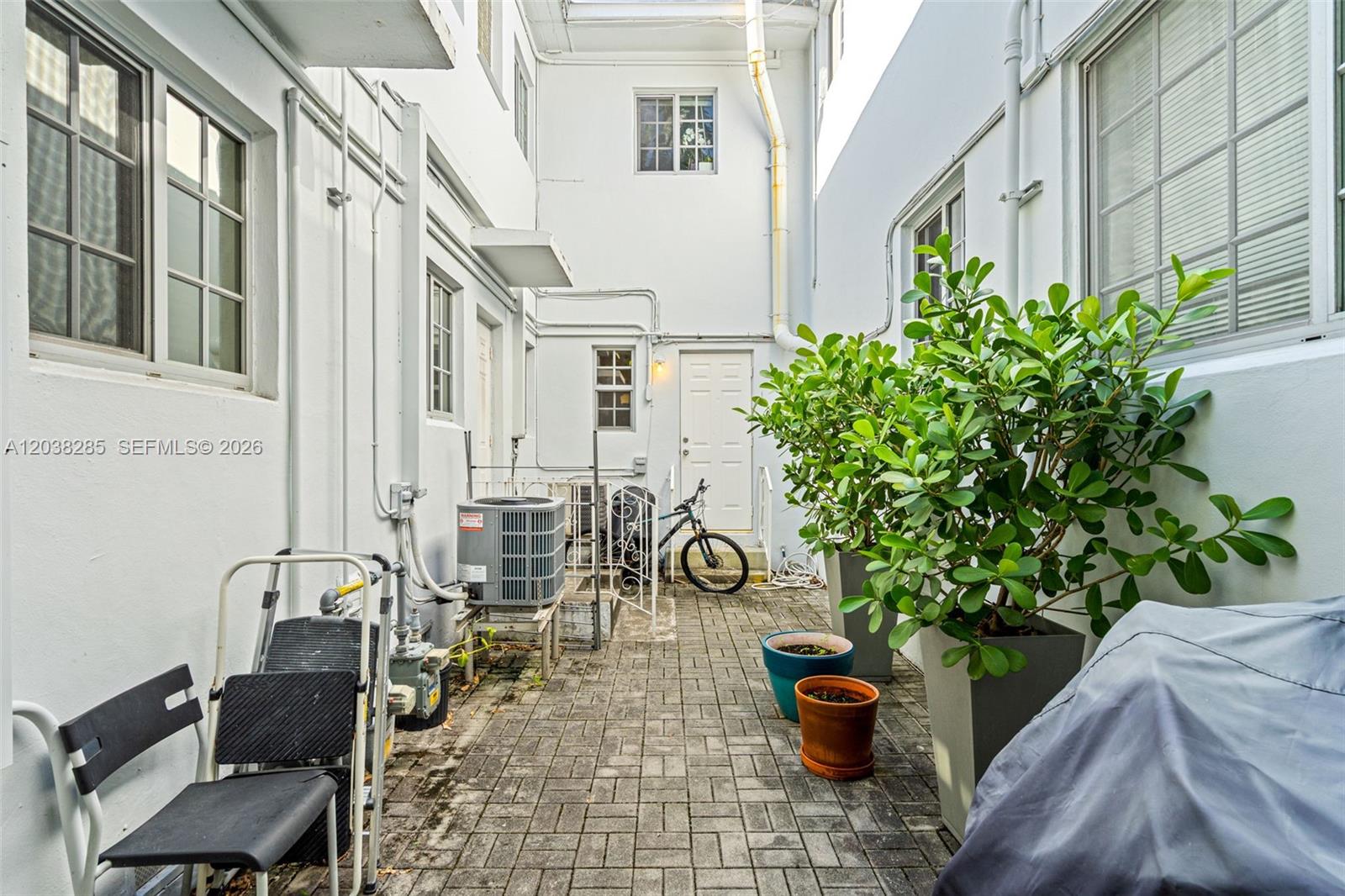 A paved outdoor courtyard features white walls, potted plants, an air conditioning unit, and a bicycle — 840 Lenox Ave # 3, Miami Beach FL 33139, MIAMI BEACH, FL