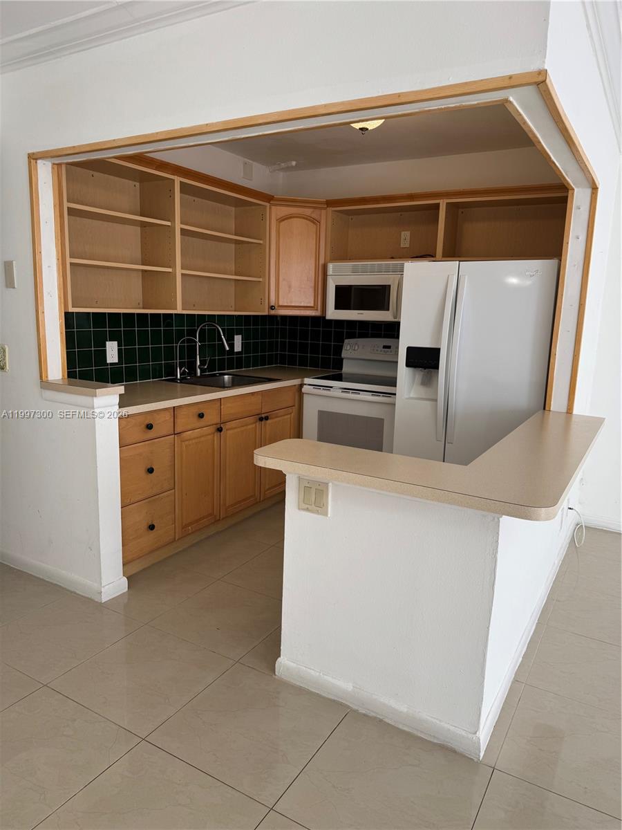 A kitchen features light wood cabinets, open shelving, a dark green tile backsplash, and white appliances — 162 Westbury J # 162, Deerfield Beach FL 33442, DEERFIELD BEACH, FL