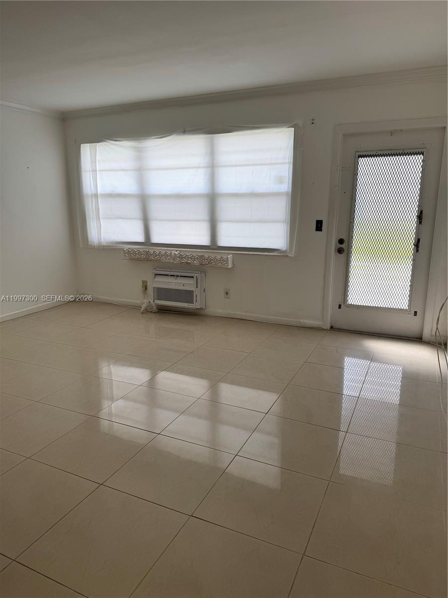 This room features light-colored tile flooring, a window with blinds, a wall-mounted air conditioner, and a door — 162 Westbury J # 162, Deerfield Beach FL 33442, DEERFIELD BEACH, FL