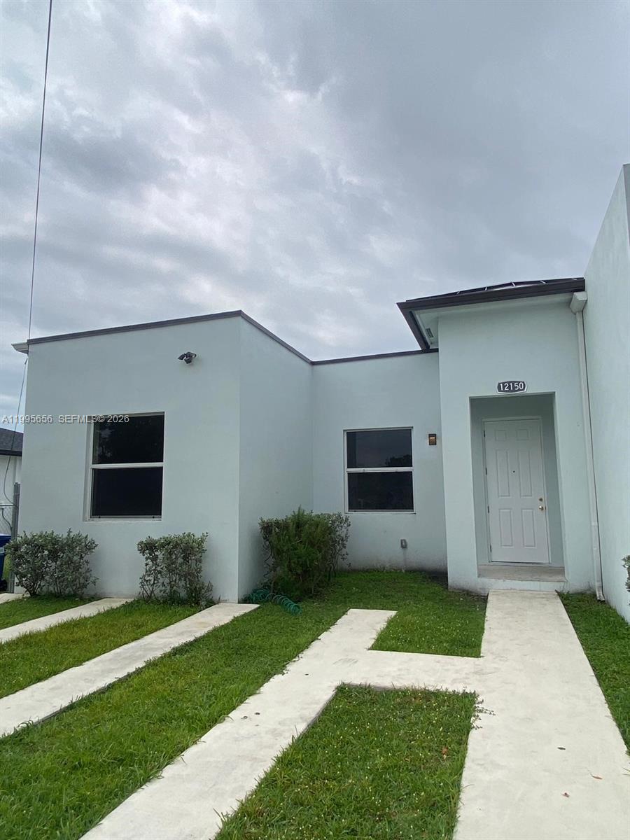The exterior of a light-colored, single-story house features a concrete walkway and a front door — 12150 SW 213th St # 12150, Miami FL 33177, MIAMI, FL