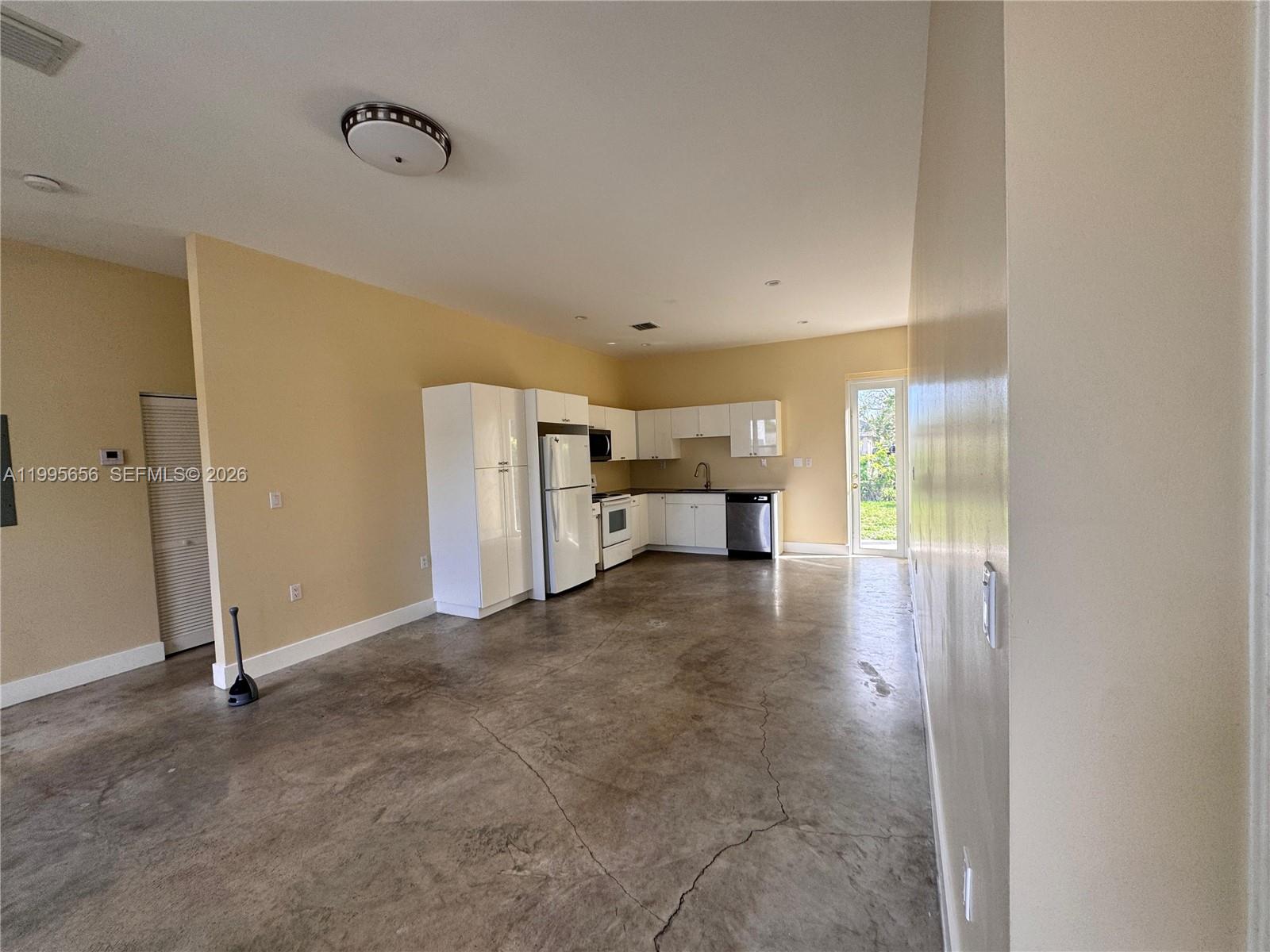 A kitchen with white cabinets and stainless steel appliances features a stained concrete floor — 12150 SW 213th St # 12150, Miami FL 33177, MIAMI, FL