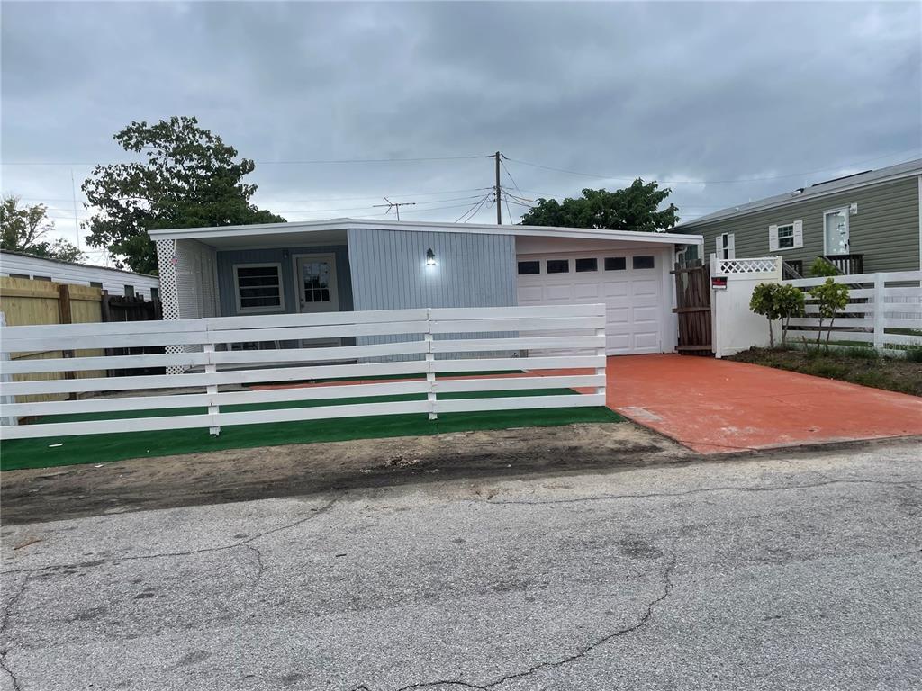A single-story house with a white fence, orange driveway, and attached garage under a cloudy sky — 2135 ORANGE DRIVE, HOLIDAY, FL