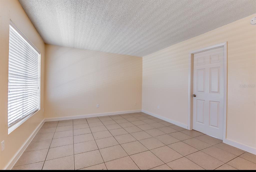 An empty room with beige walls, light-colored tile flooring, a window with blinds, and a door — 4410 N HALE AVENUE, TAMPA, FL