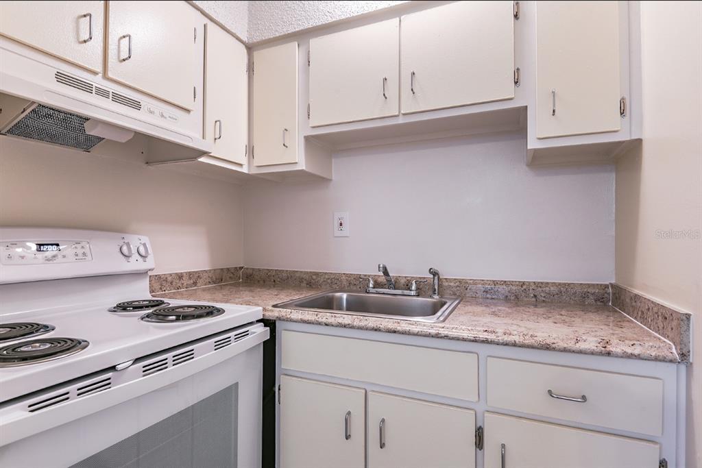 A kitchen features white cabinets, a granite-look countertop, a stainless steel sink, and a stove — 4410 N HALE AVENUE, TAMPA, FL
