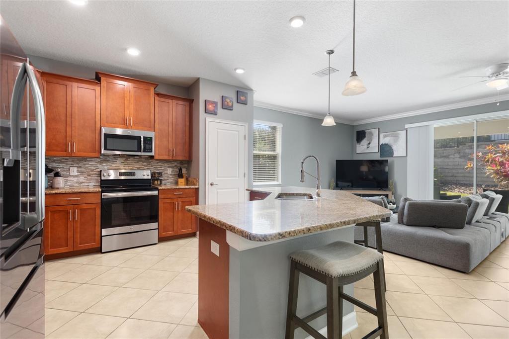 A kitchen with wood cabinets and granite countertops overlooks a living area with gray furniture — 1414 CLUBMAN DR, DAVENPORT, FL