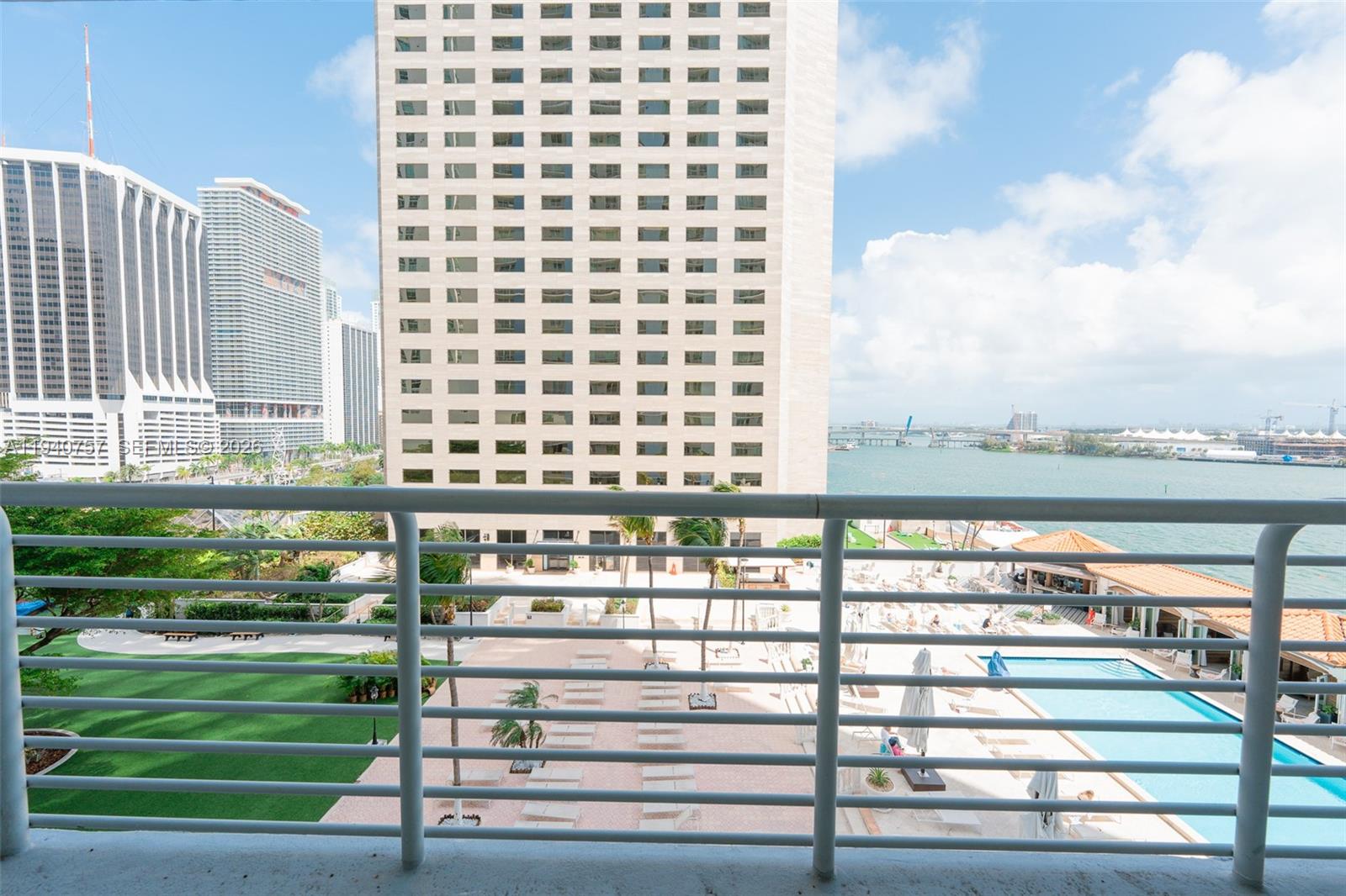 A balcony view overlooks a swimming pool, a grassy area, and high-rise buildings near water — 335 S Biscayne Blvd # 1108, Miami FL 33131, MIAMI, FL