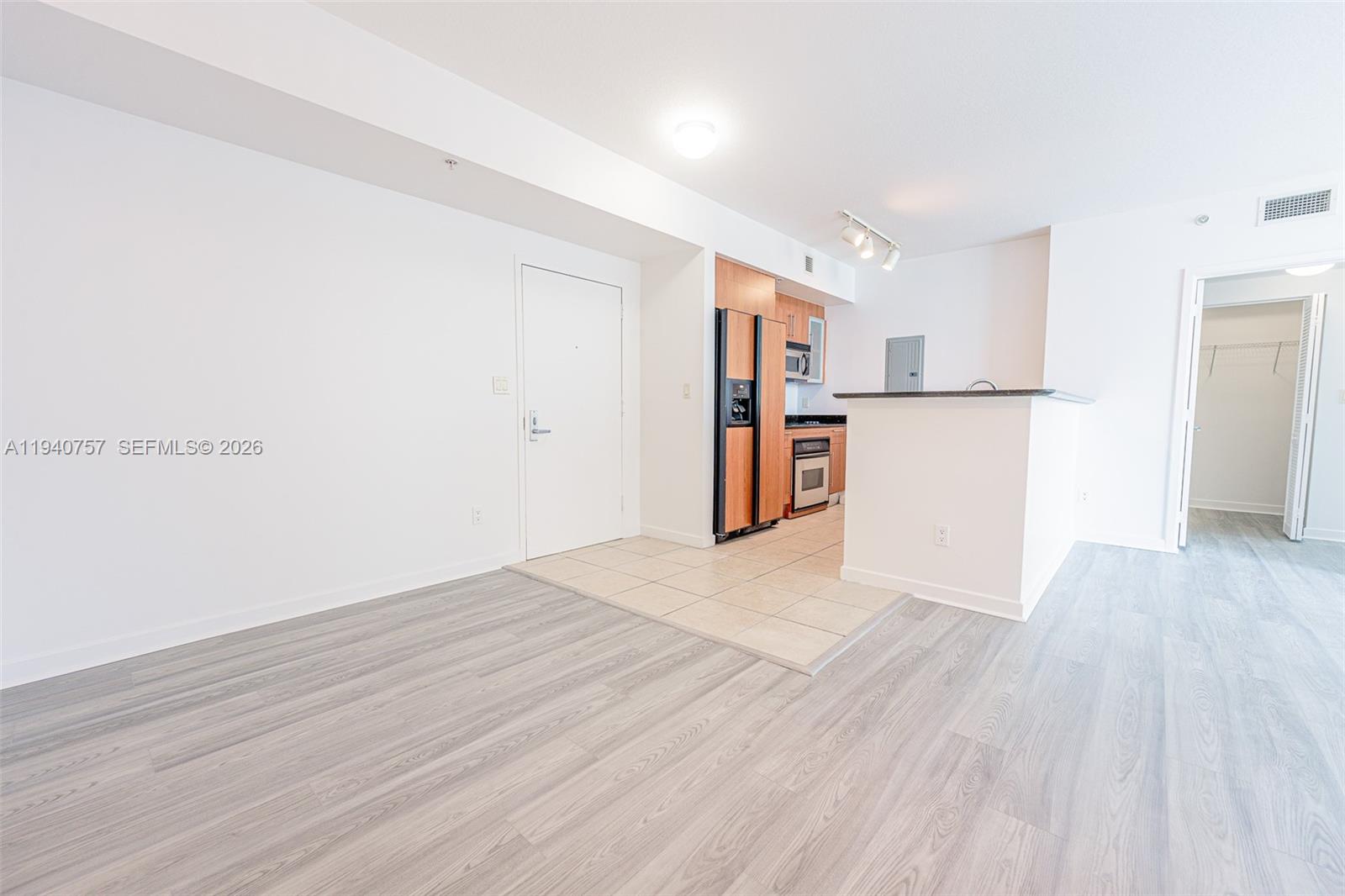 An open-concept living area features light wood-look flooring, a tiled kitchen entry, and white walls — 335 S Biscayne Blvd # 1108, Miami FL 33131, MIAMI, FL