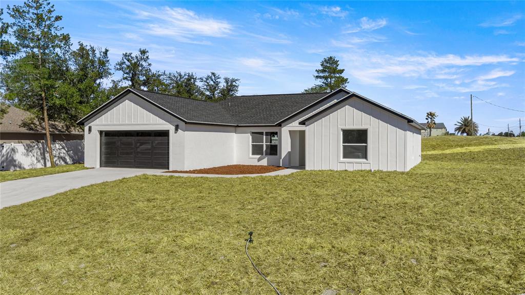 A single-story house with white board-and-batten siding, a dark roof, and a two-car garage — 9989 SW 42ND AVENUE, OCALA, FL