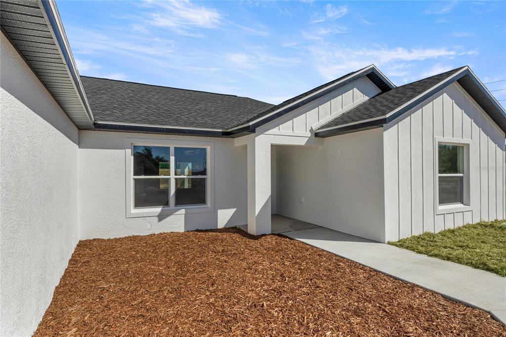 The exterior of a modern house features white stucco and board-and-batten siding with mulch landscaping — 9989 SW 42ND AVENUE, OCALA, FL