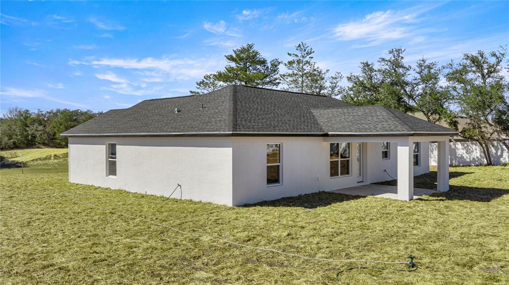 The exterior rear view of a single-story house with a covered patio and lawn — 9989 SW 42ND AVENUE, OCALA, FL