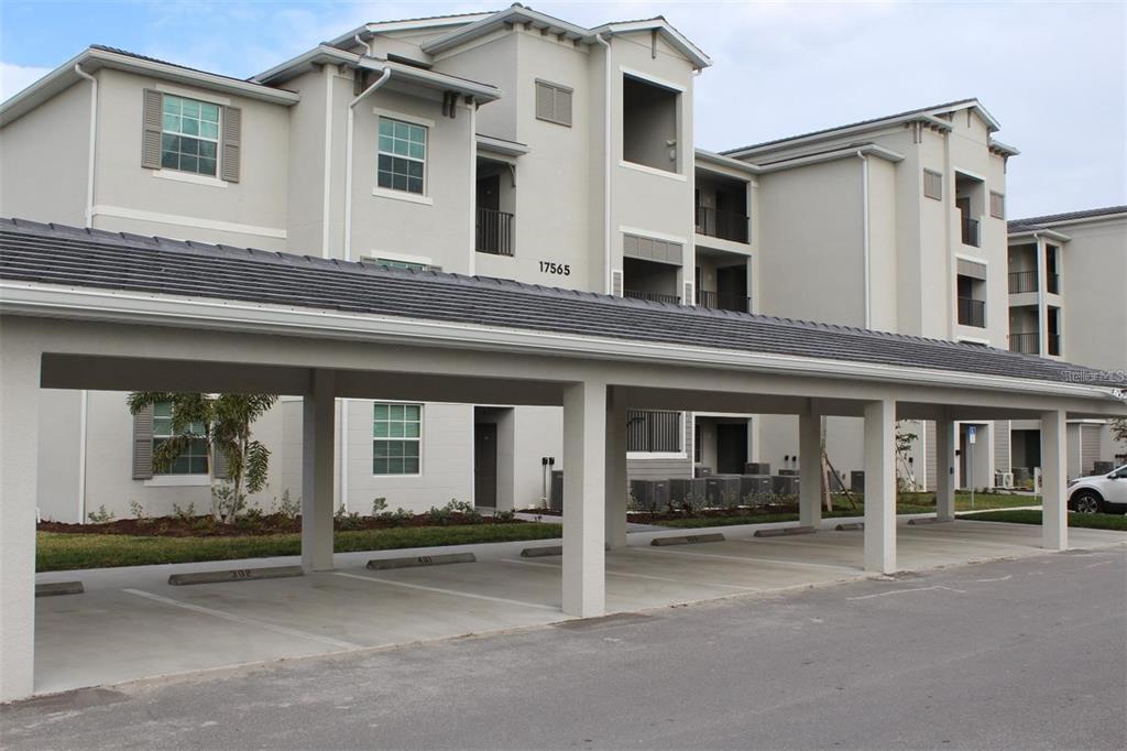 A multi-story apartment building with a covered parking structure in the foreground — 17565 OPAL SAND DRIVE UNIT 401, VENICE, FL