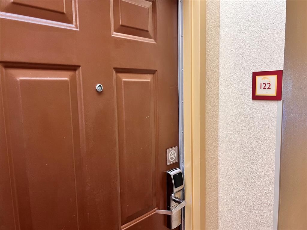 A brown door with a digital lock and a room number sign labeled 122 — 3000 MAINGATE LANE UNIT 122, KISSIMMEE, FL