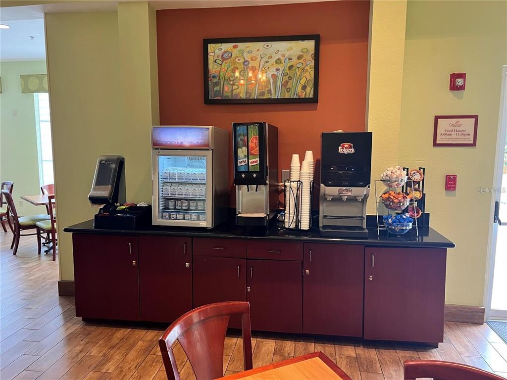 A hotel breakfast station features a beverage cooler, juice dispenser, coffee machine, and snack rack — 3000 MAINGATE LANE UNIT 122, KISSIMMEE, FL
