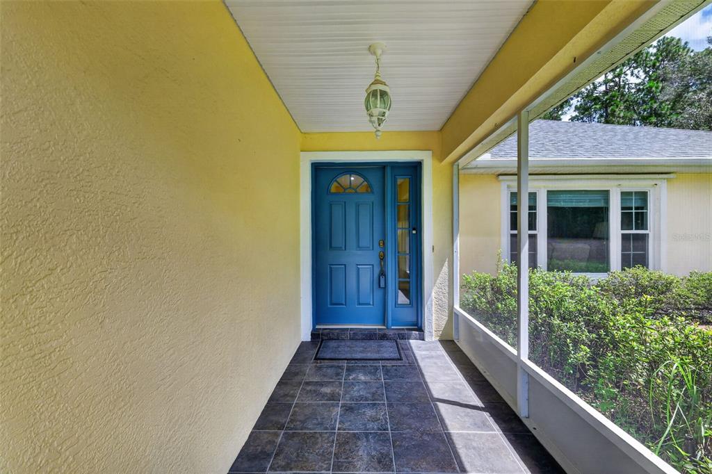 A covered entryway with a blue front door, tiled floor, and yellow exterior walls — 21859 SW 82ND STREET, DUNNELLON, FL