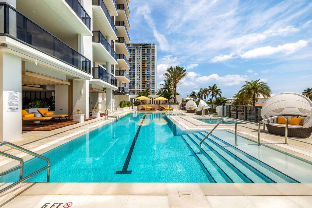 A modern swimming pool with lounge chairs and cabanas sits beside a multi-story apartment building — 305 Briny Avenue # 706, Pompano Beach FL 33062, POMPANO BEACH, FL