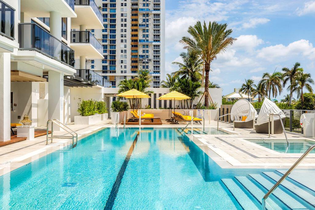 A swimming pool with lounge chairs and umbrellas sits on a patio beside a building — 305 Briny Avenue # 706, Pompano Beach FL 33062, POMPANO BEACH, FL