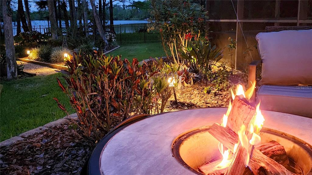 A fire pit burns on a patio overlooking a backyard with landscaping and a lake — 2021 WATERFORD ESTATES DRIVE, NEW SMYRNA BEACH, FL