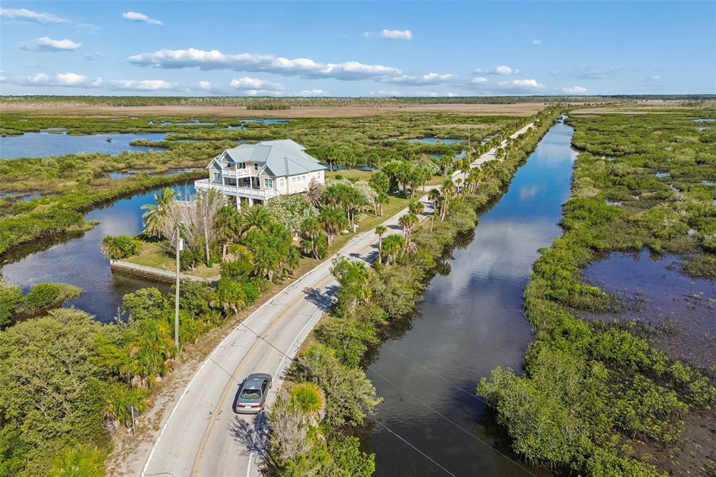 An aerial view shows a house situated on a marshy landscape beside a paved road — 10501 PINE ISLAND DRIVE, WEEKI WACHEE, FL