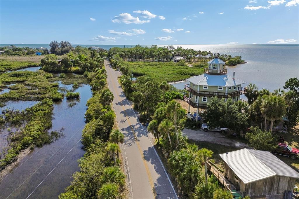 An aerial view shows a coastal road, marshland, and a multi-story house on stilts — 10501 PINE ISLAND DRIVE, WEEKI WACHEE, FL