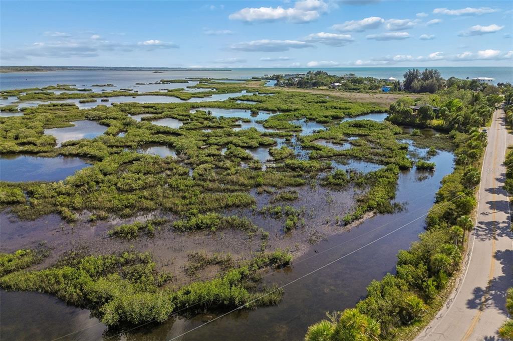 An aerial view shows a coastal road running alongside a large, marshy mangrove wetland area — 10501 PINE ISLAND DRIVE, WEEKI WACHEE, FL