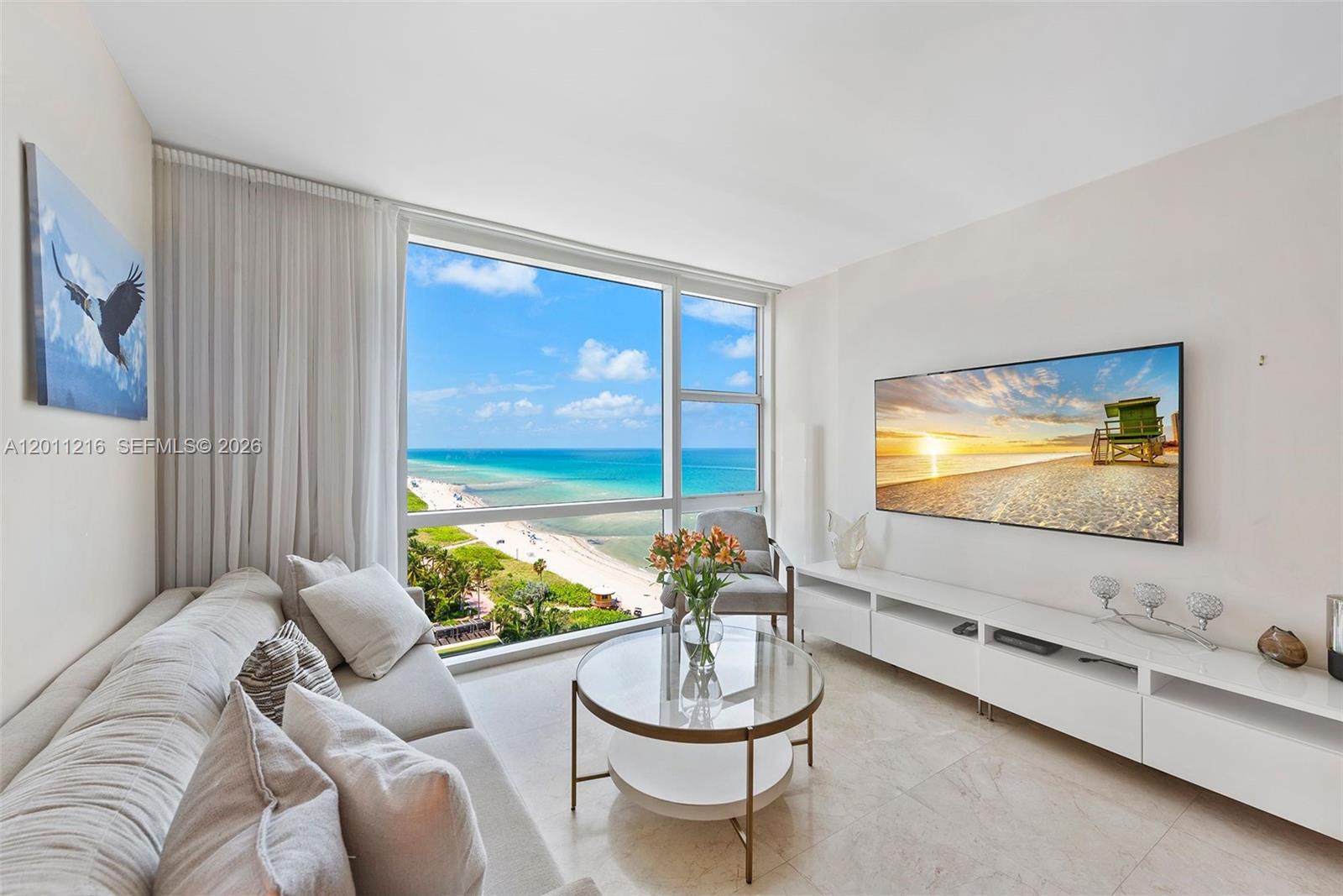 A living room features a large window with ocean views, a sofa, and a television — 6801 Collins Ave # 1203, Miami Beach FL 33141, MIAMI BEACH, FL