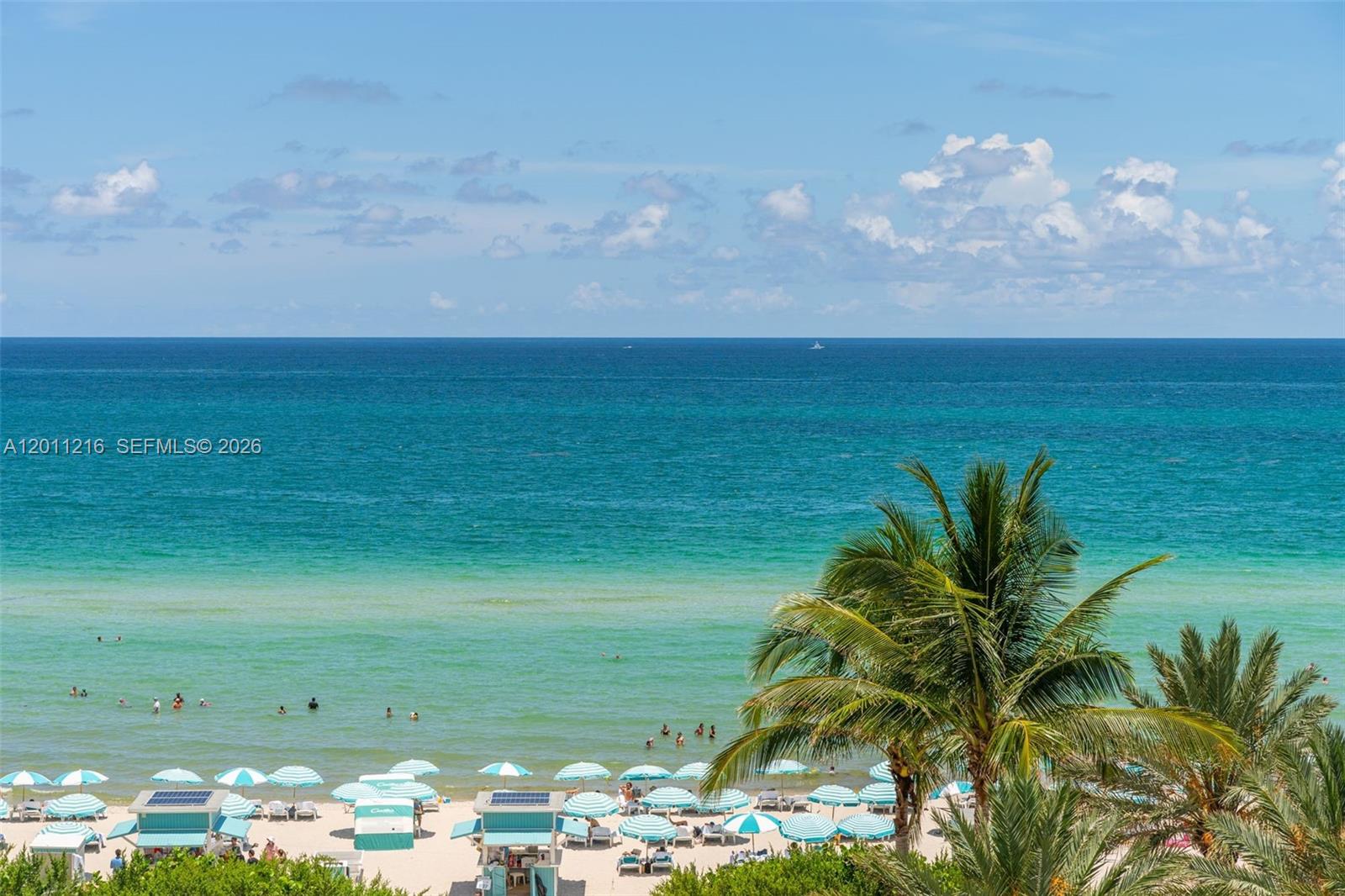 A high-angle view of a sandy beach with umbrellas, palm trees, and the ocean — 6801 Collins Ave # 1203, Miami Beach FL 33141, MIAMI BEACH, FL
