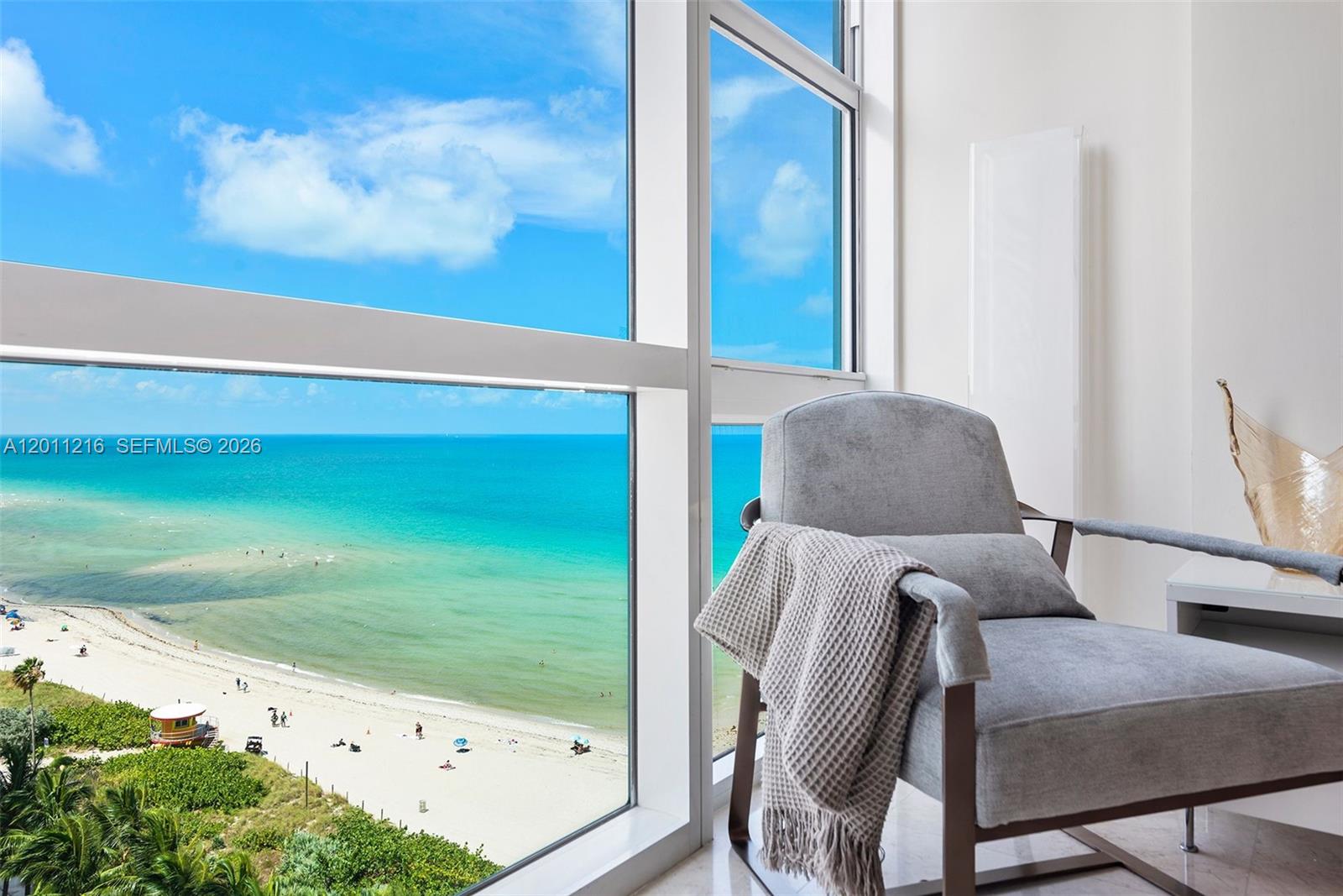 A gray armchair sits beside a large window overlooking a beach and the ocean — 6801 Collins Ave # 1203, Miami Beach FL 33141, MIAMI BEACH, FL