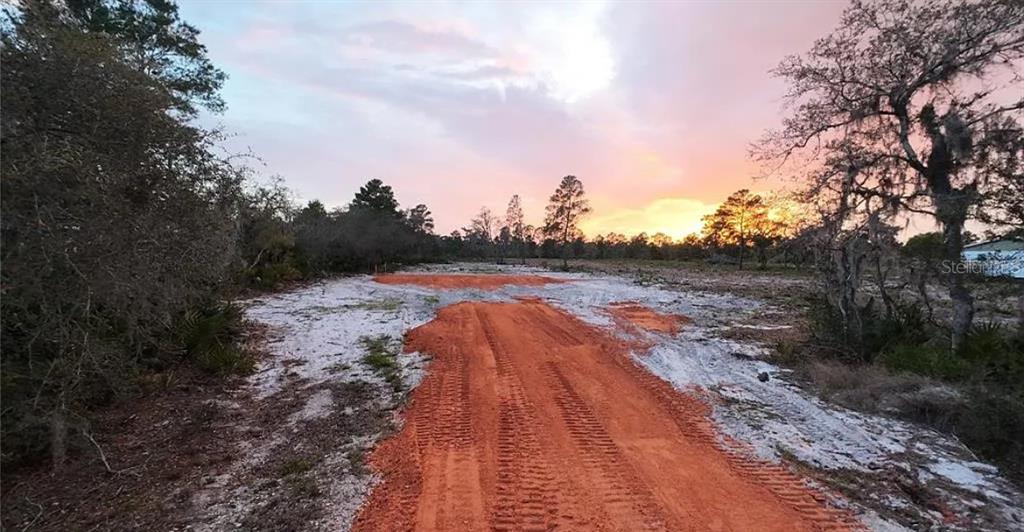 A dirt path leads through a cleared, sandy lot toward a sunset sky — WOODSTORK WAY, FROSTPROOF, FL