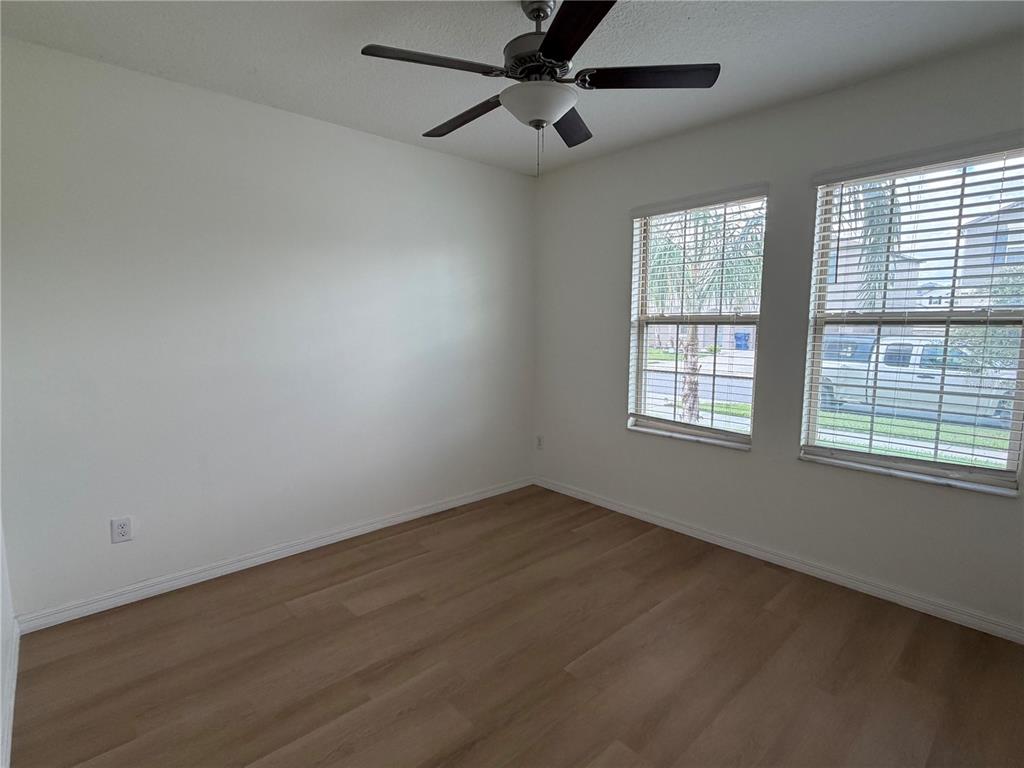 An empty bedroom features light wood-look flooring, white walls, a ceiling fan, and two windows — 31823 SUN KETTLE LOOP, WESLEY CHAPEL, FL