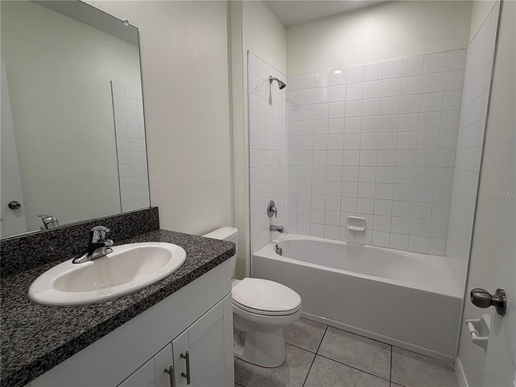 A bathroom features a white vanity with a granite countertop, toilet, and tiled shower-tub combo — 31823 SUN KETTLE LOOP, WESLEY CHAPEL, FL