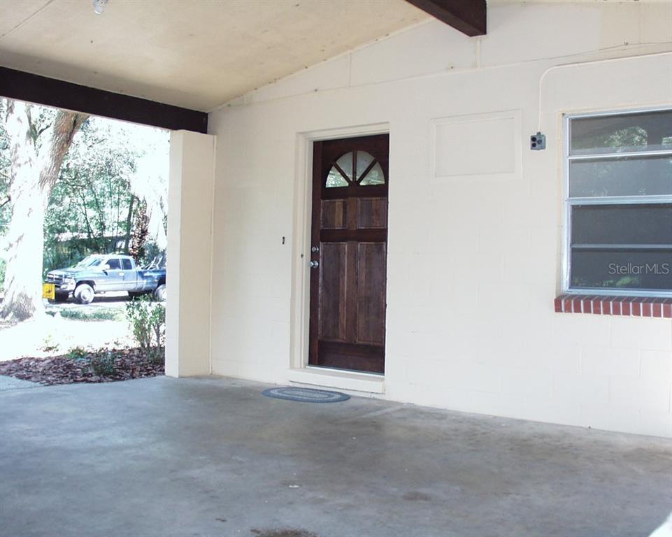 A covered concrete carport leads to a dark wood front door with a glass insert — 621 NW 36TH DRIVE, GAINESVILLE, FL