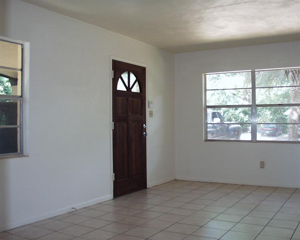 An empty room with white walls, tiled floors, a wooden front door, and two windows — 621 NW 36TH DRIVE, GAINESVILLE, FL
