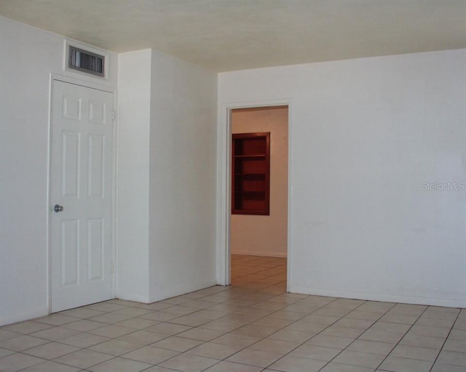 A room with white walls and tiled floors features a closed door and an open doorway — 621 NW 36TH DRIVE, GAINESVILLE, FL