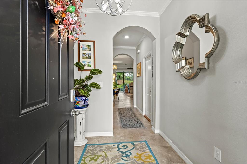 A view from an open black front door into a tiled foyer with an arched hallway — 2455 MIDNIGHT PEARL DRIVE, SARASOTA, FL