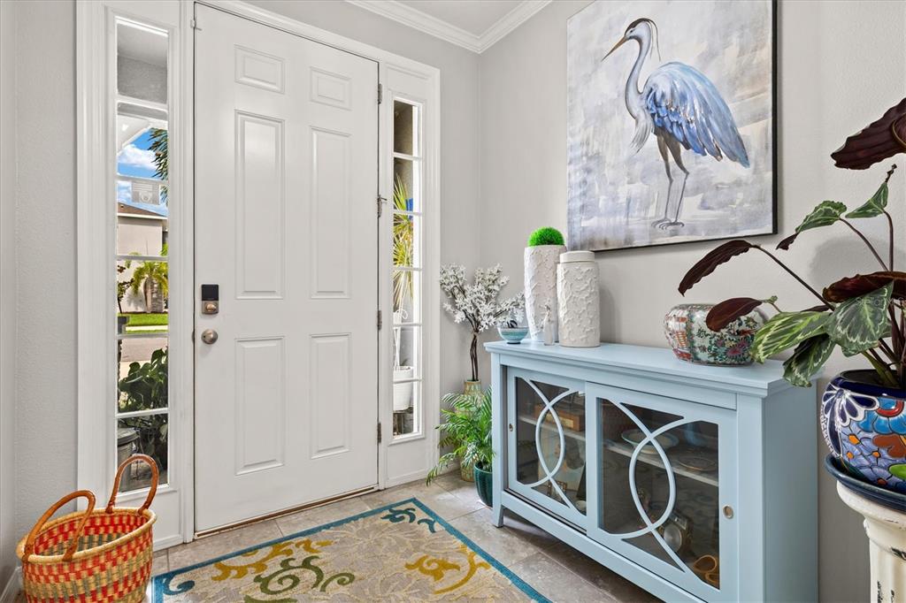 A light-filled entryway features a white door, a blue console table, and a heron painting — 2455 MIDNIGHT PEARL DRIVE, SARASOTA, FL