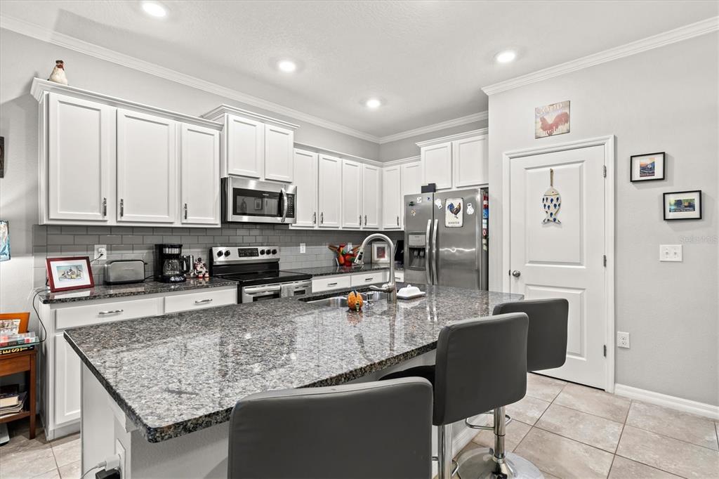 A kitchen features white cabinets, granite countertops, a central island with bar stools, and stainless-steel appliances — 2455 MIDNIGHT PEARL DRIVE, SARASOTA, FL