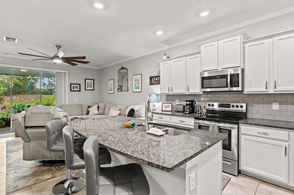 A kitchen with white cabinets and granite countertops overlooks a living area with a sectional — 2455 MIDNIGHT PEARL DRIVE, SARASOTA, FL