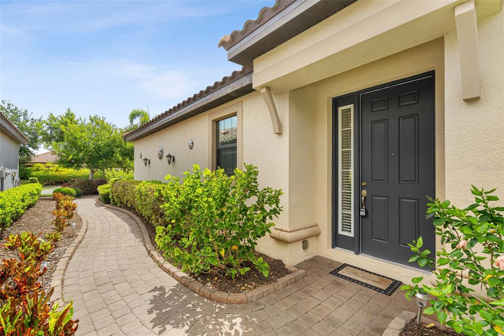 A paved walkway leads to the dark front door of a beige stucco house — 10205 SAINT FRANCIS TERRACE, PALMETTO, FL