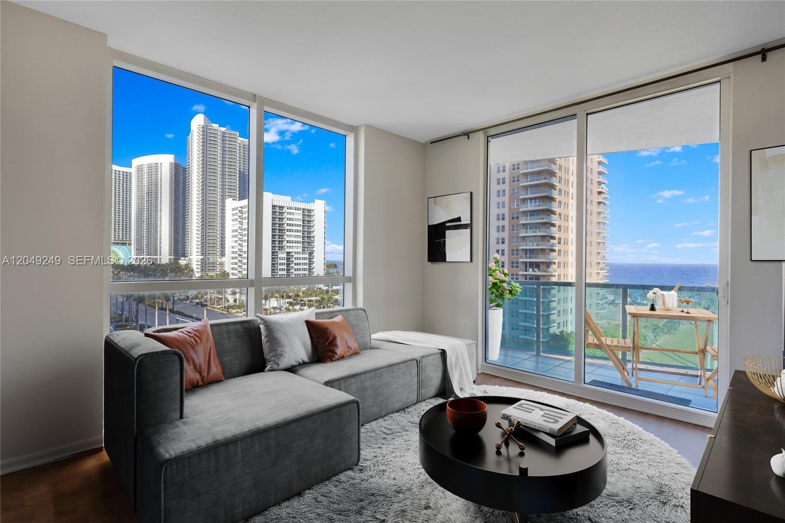A living room features a grey sectional sofa, a round coffee table, and floor-to-ceiling windows — 1945 S Ocean Dr # 714, Hallandale Beach FL 33009, HALLANDALE BEACH, FL