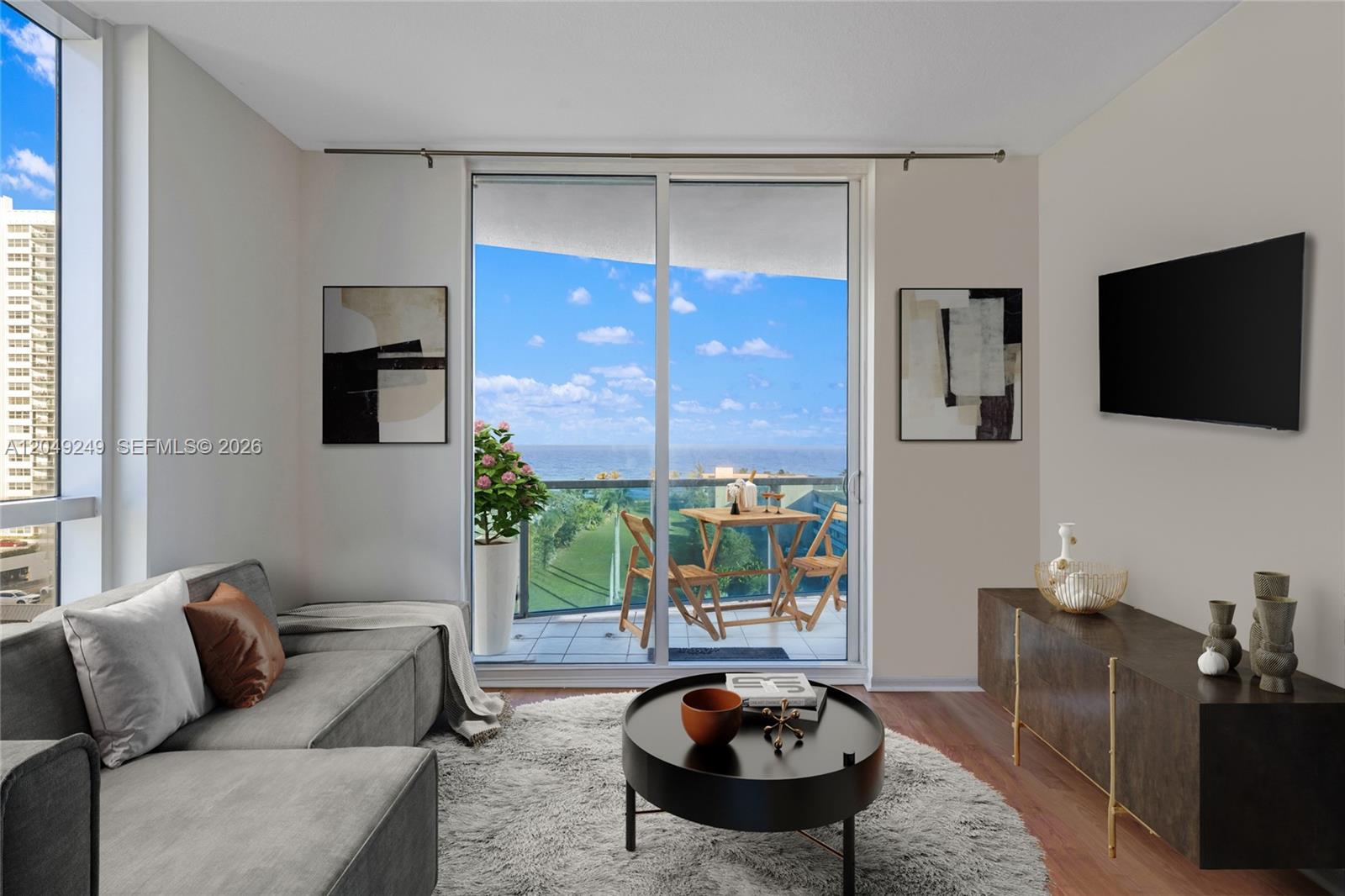 A living room features a grey sectional sofa, circular coffee table, and balcony with ocean views — 1945 S Ocean Dr # 714, Hallandale Beach FL 33009, HALLANDALE BEACH, FL
