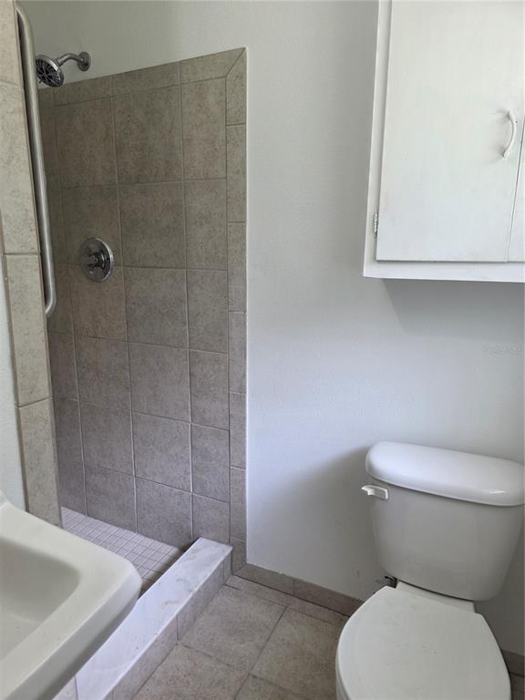 A bathroom featuring a tiled walk-in shower, a white toilet, and a wall-mounted cabinet — 507 NE 21ST TERRACE, OCALA, FL