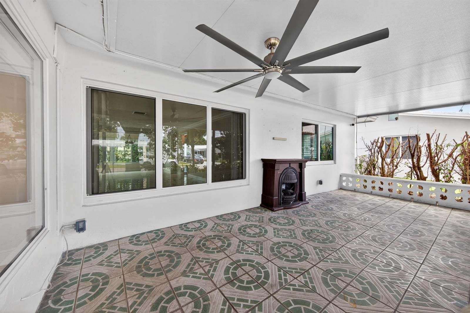 A covered patio features patterned tile flooring, a large ceiling fan, and a decorative fireplace — 391 Leisure Boulevard, Pompano Beach FL 33064, POMPANO BEACH, FL