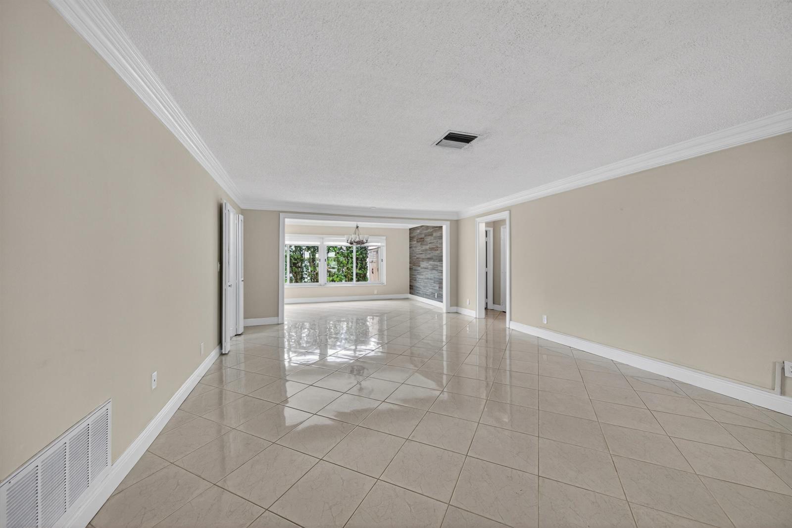 An empty room with beige walls, large light-colored floor tiles, and a windowed dining area — 391 Leisure Boulevard, Pompano Beach FL 33064, POMPANO BEACH, FL