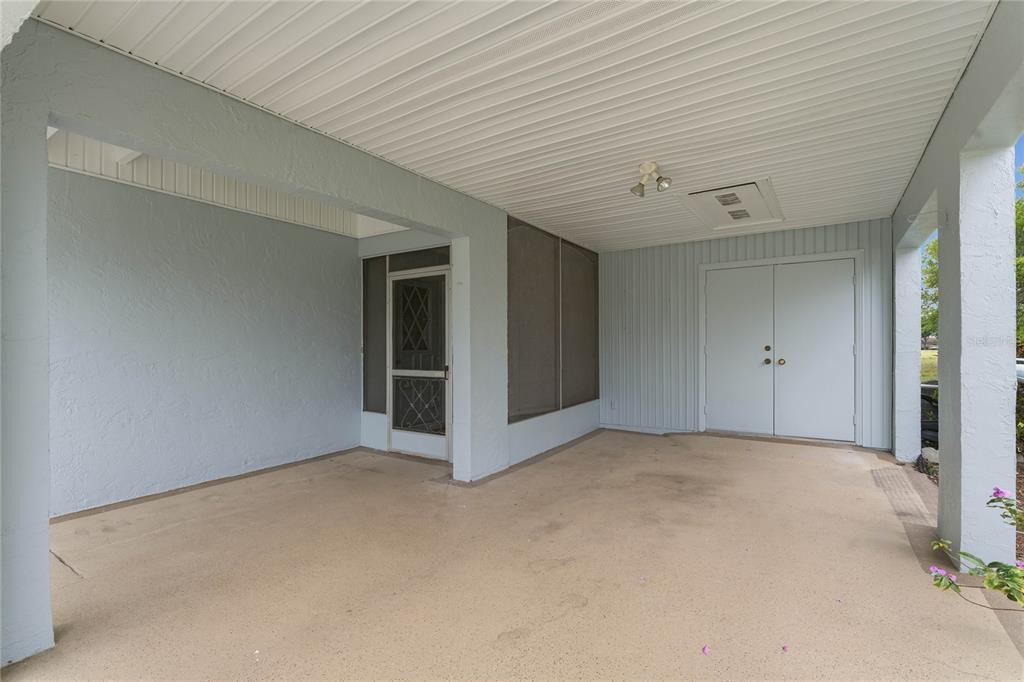 A covered concrete carport features a screen door, double entry doors, and light blue walls — 417 GLADSTONE PLACE, SUN CITY CENTER, FL