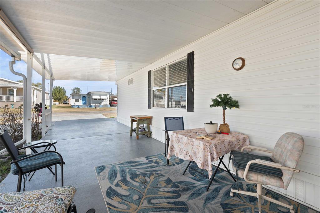 A covered concrete patio features outdoor furniture, a patterned rug, and a white exterior wall — 37332 SANDRA AVENUE, ZEPHYRHILLS, FL