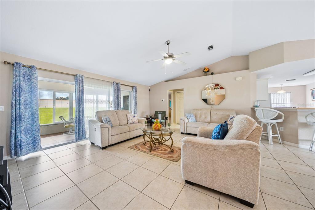 A living room with beige tile floors, neutral furniture, and a sliding glass door to a patio — 140 MORNING GLORY CIRCLE, WINTER HAVEN, FL